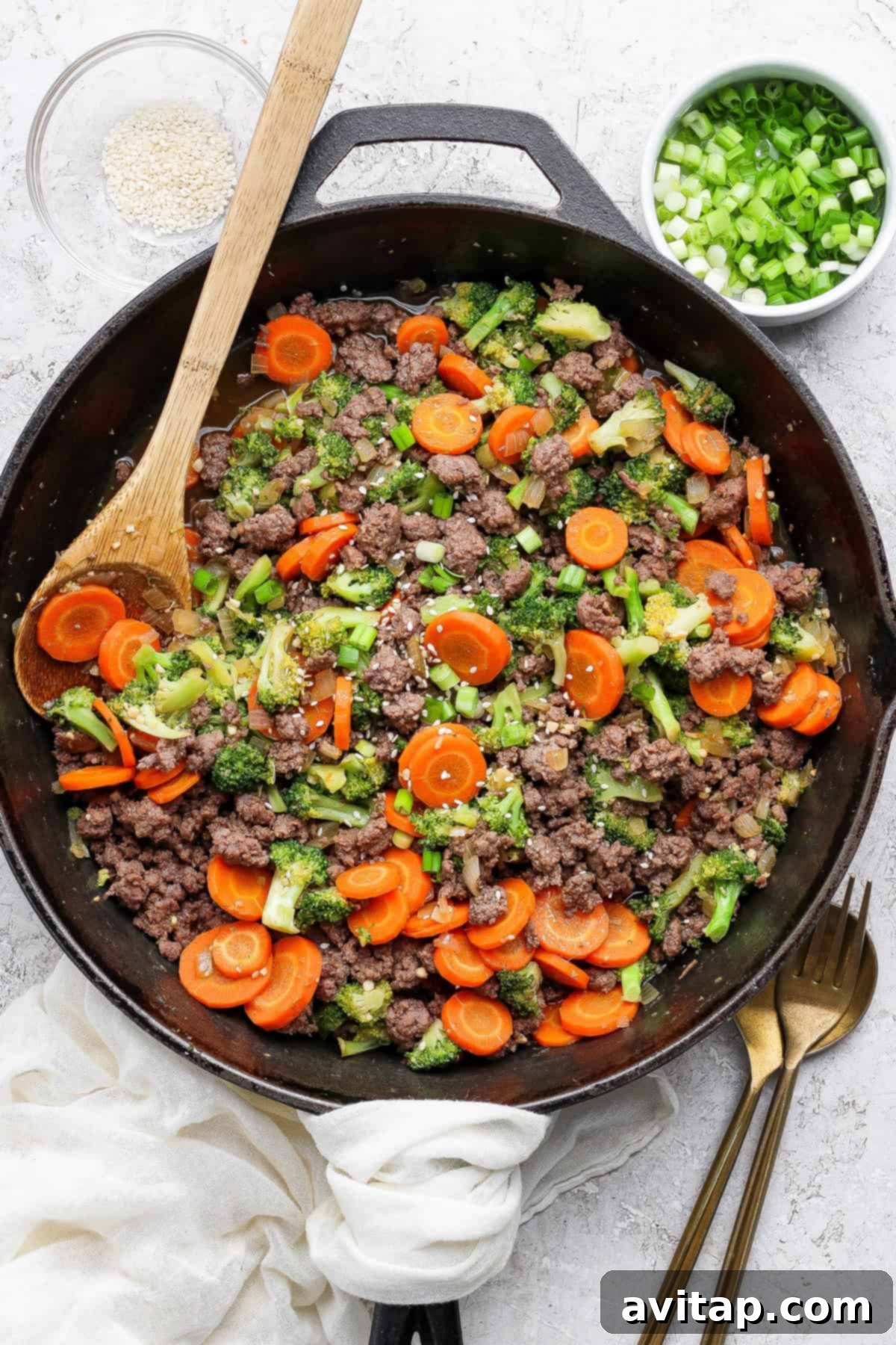 Ground Beef with Broccoli Florets 6 Ground beef and broccoli dish garnished with green onions and sesame seeds in a cast iron skillet.