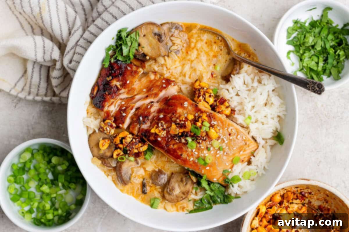 A delicious bowl of Chili Crunch Salmon with Creamy Coconut Brothy Rice, featuring rice, salmon, mushrooms, nuts, sesame seeds, and herbs.