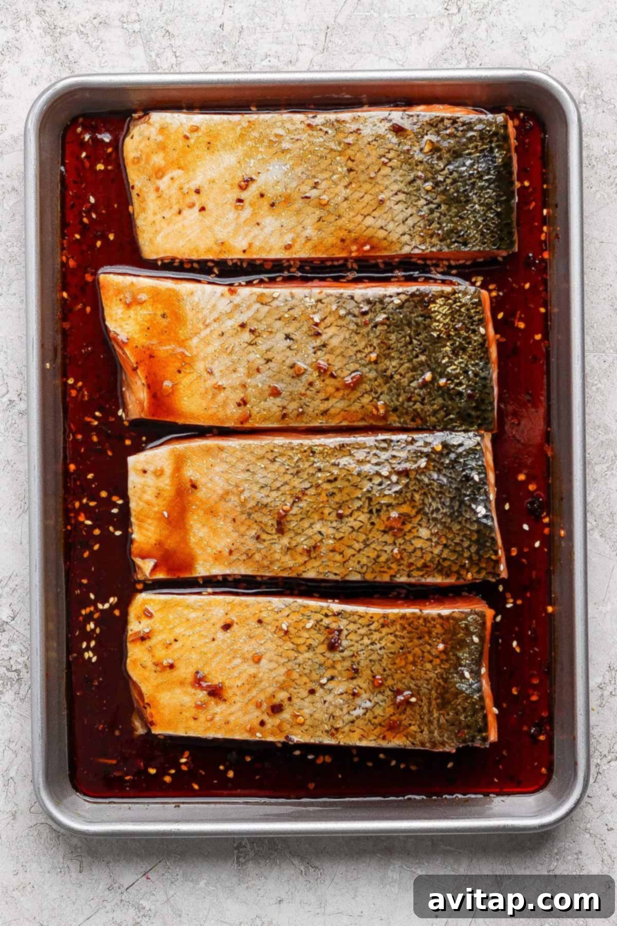 Raw salmon fillets marinating in a dark sauce with spices.