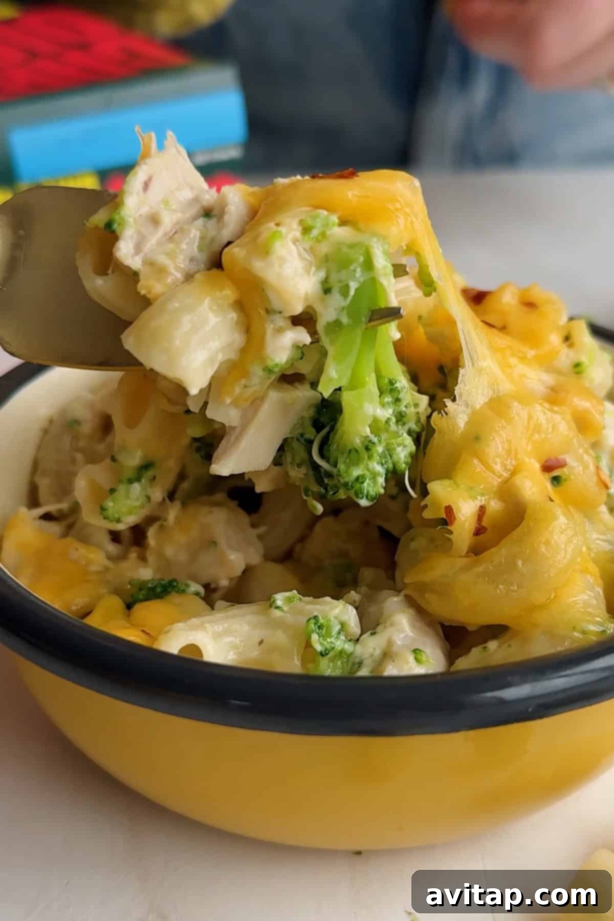 A fork lifting a portion of cheesy pasta with broccoli and chicken.