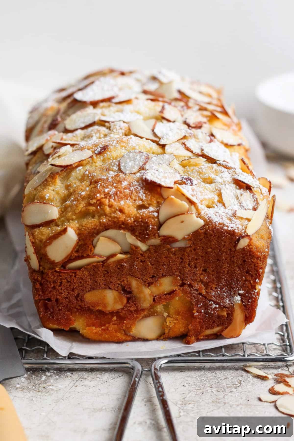 Finished almond croissant cottage cheese pull-apart bread cooling on a rack, alongside a knife and parchment paper, ready to be sliced and enjoyed.