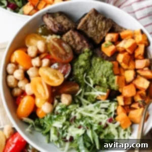 High-Protein Trader Joe's Meal Ideas 11 A bowl filled with grilled beef strips, roasted sweet potatoes, cherry tomatoes, chickpeas, shredded greens, and green sauce, with a fork and another bowl partially visible.