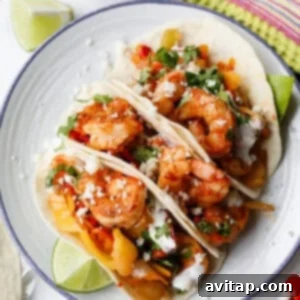 High-Protein Trader Joe's Meal Ideas 8 Three shrimp tacos with diced vegetables, cilantro, crumbled cheese, and sauce on flour tortillas, served on a plate with lime wedges.