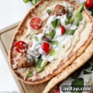 High-Protein Trader Joe's Meal Ideas 9 Two flatbreads topped with meatballs, hummus, sliced cucumbers, cherry tomatoes, tzatziki sauce, fresh herbs, and feta cheese on a wooden board.
