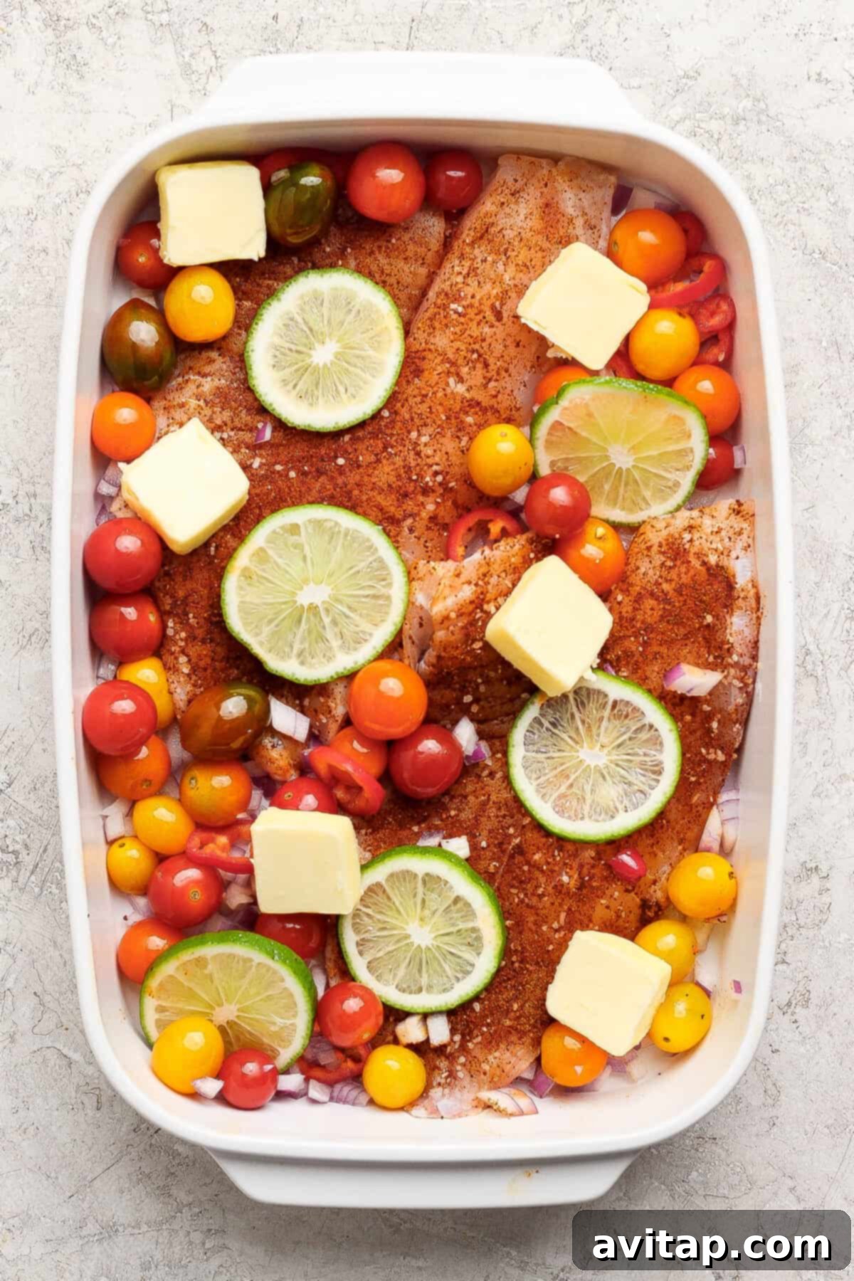 Raw fish fillets seasoned and arranged in a baking dish with vegetables.