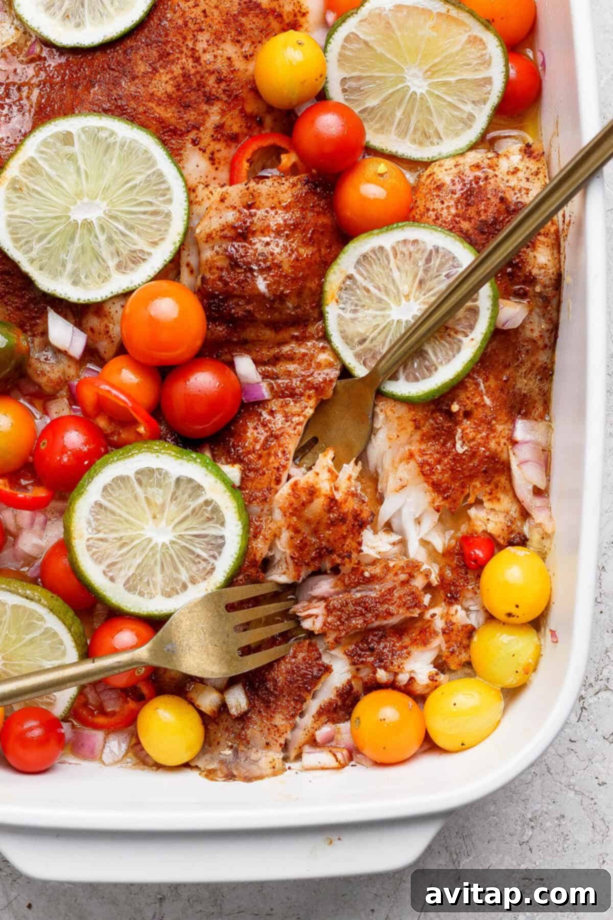 Baked fish fillets with lime, tomatoes, and onions in a baking dish.