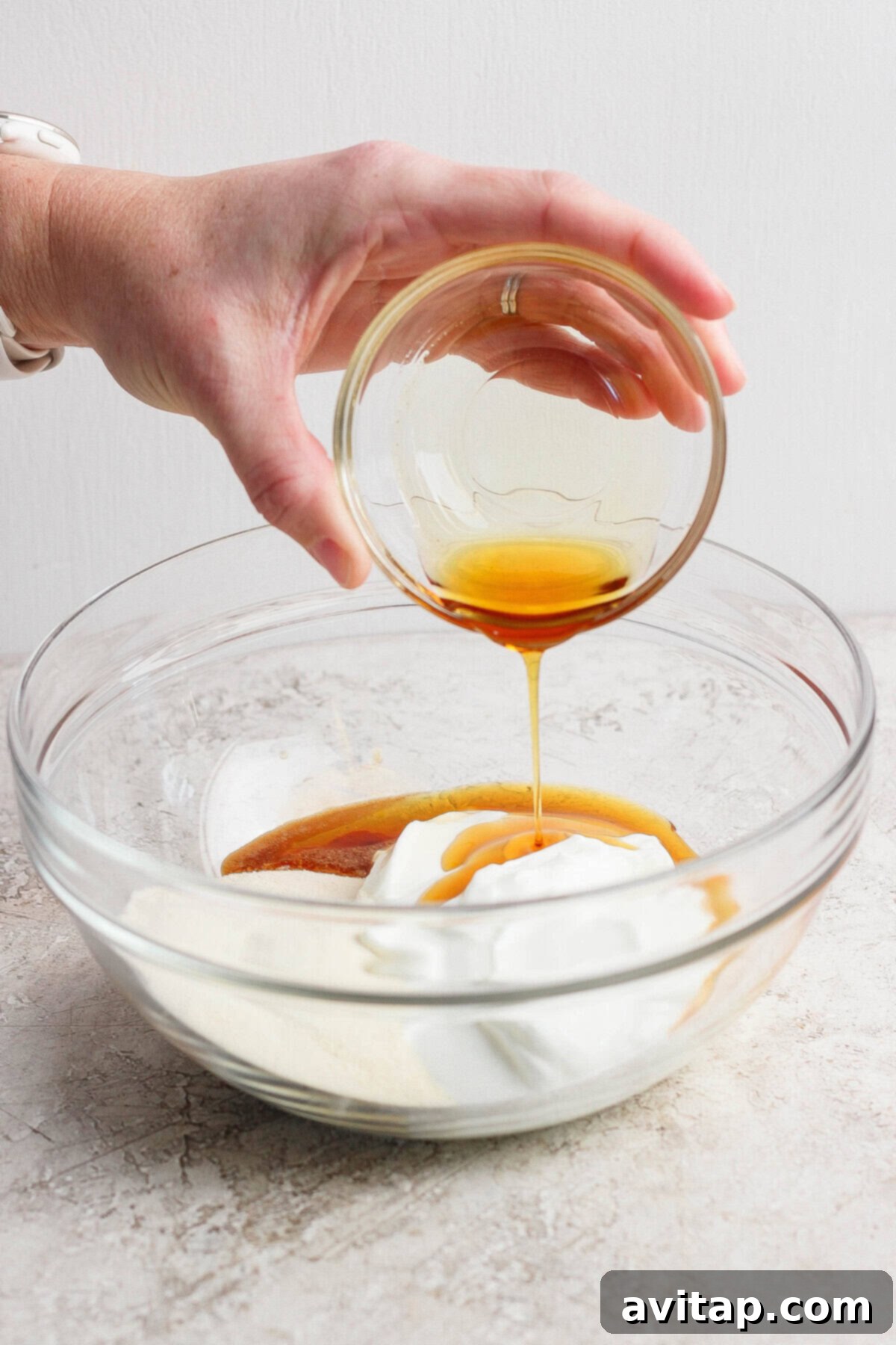 High-Protein Banana Bliss 3 Pouring maple syrup into a bowl of yogurt and protein powder