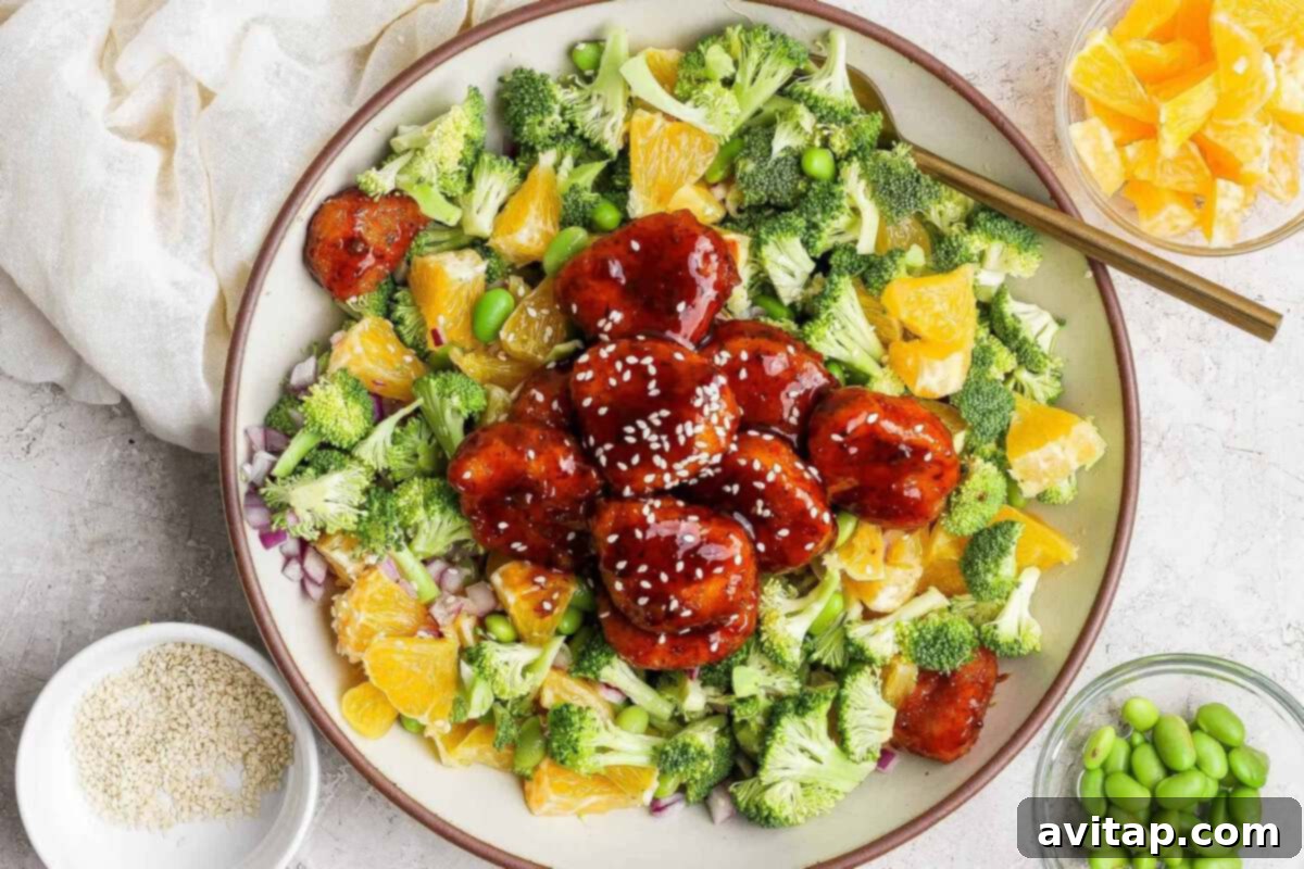 A colorful bowl of broccoli orange salad with glazed chicken teriyaki, edamame, and sesame seeds.