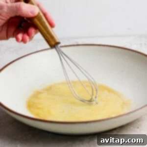 A person whisking liquids together in a white bowl.
