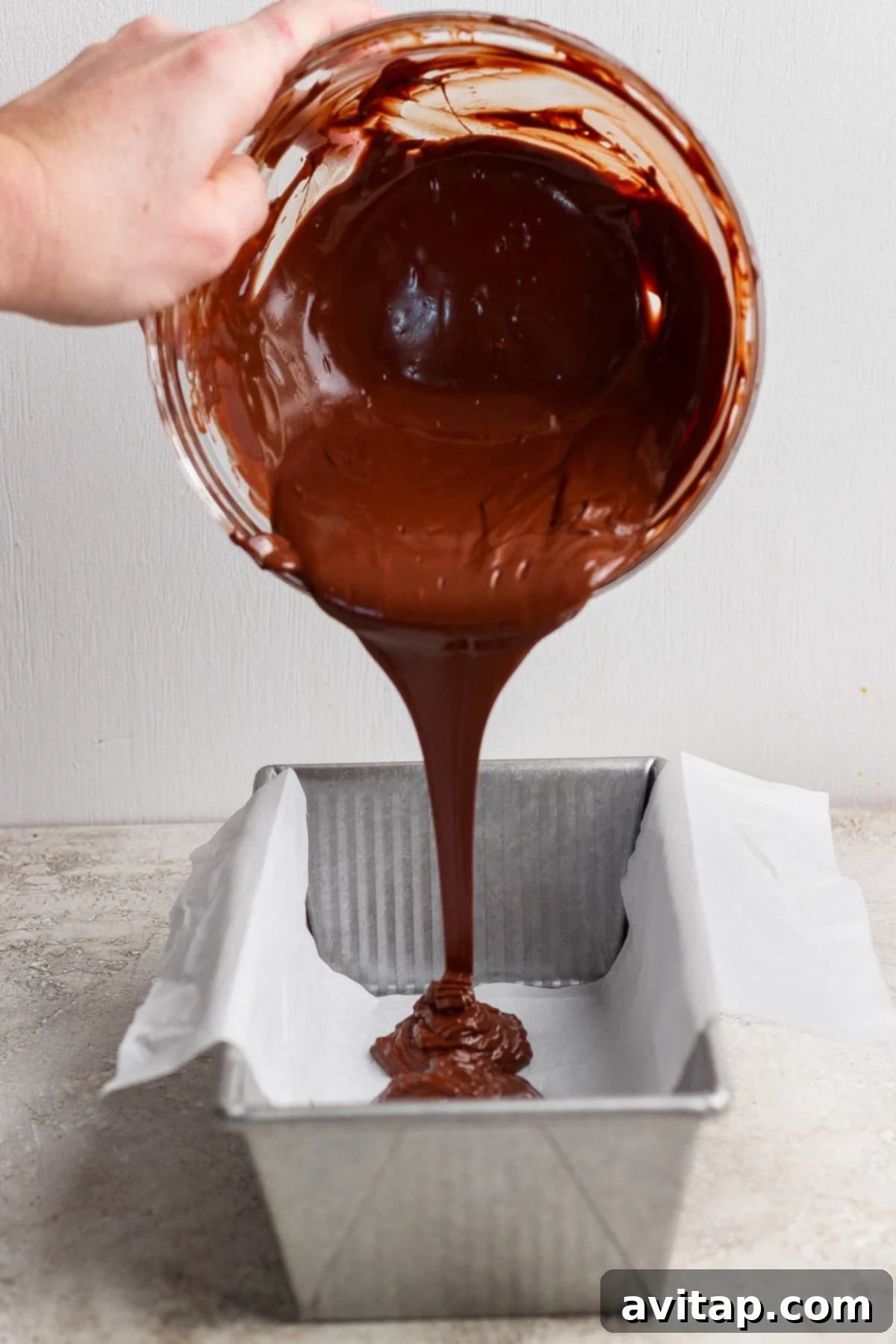 Melted chocolate being poured into a parchment-lined loaf pan.