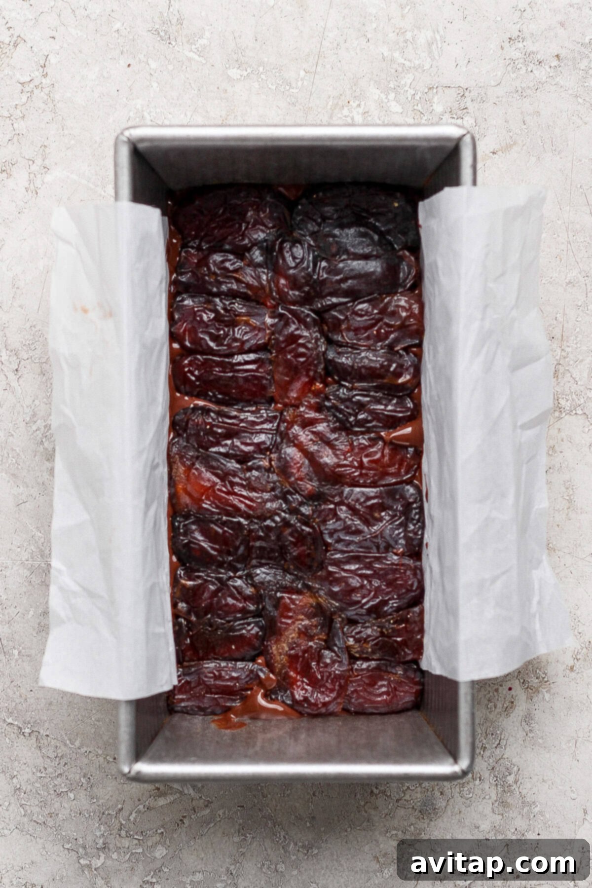 Pitted dates arranged closely together in a rectangular baking pan lined with parchment paper.