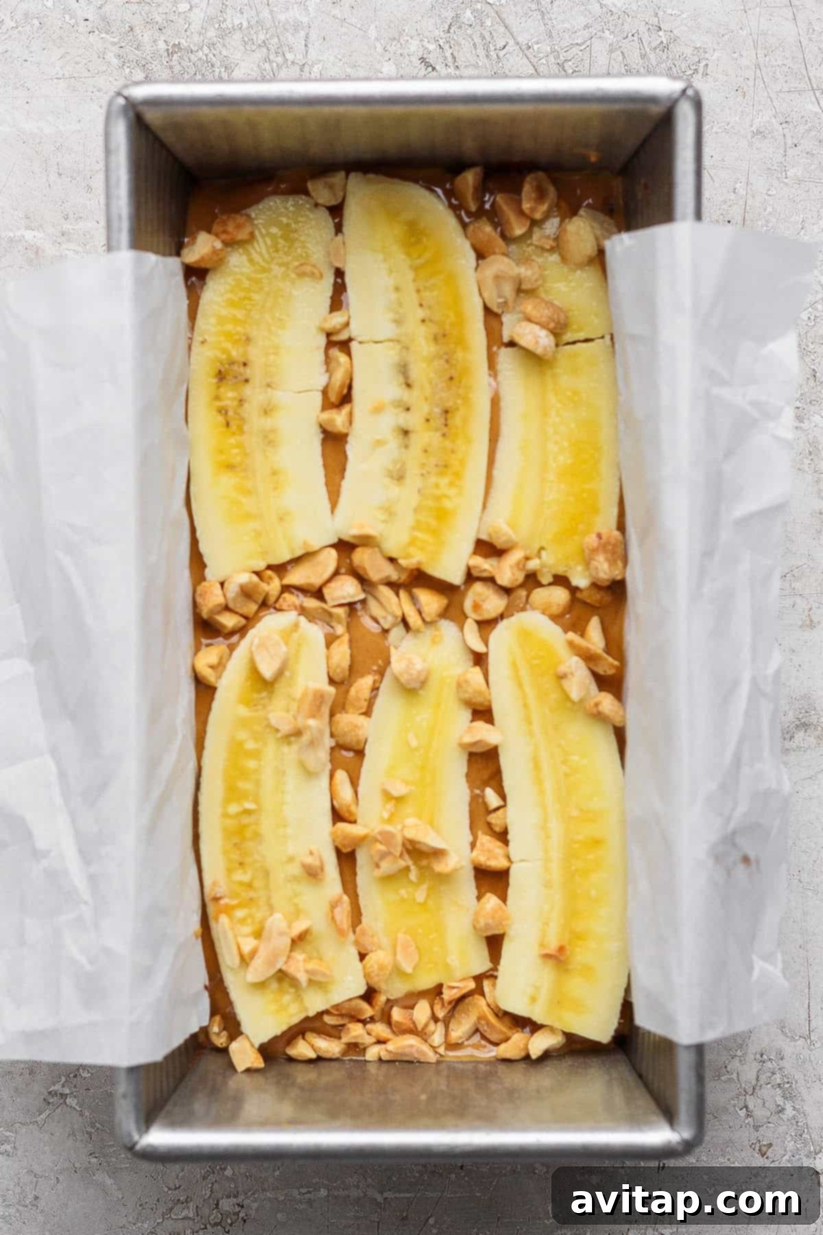 Batter topped with halved banana slices and chopped peanuts in a baking tin lined with parchment paper.