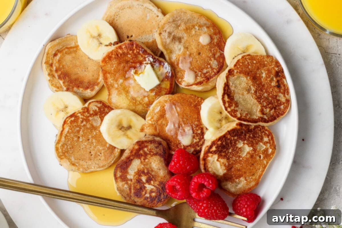 Mini pancakes topped with butter, banana slices, raspberries, and syrup