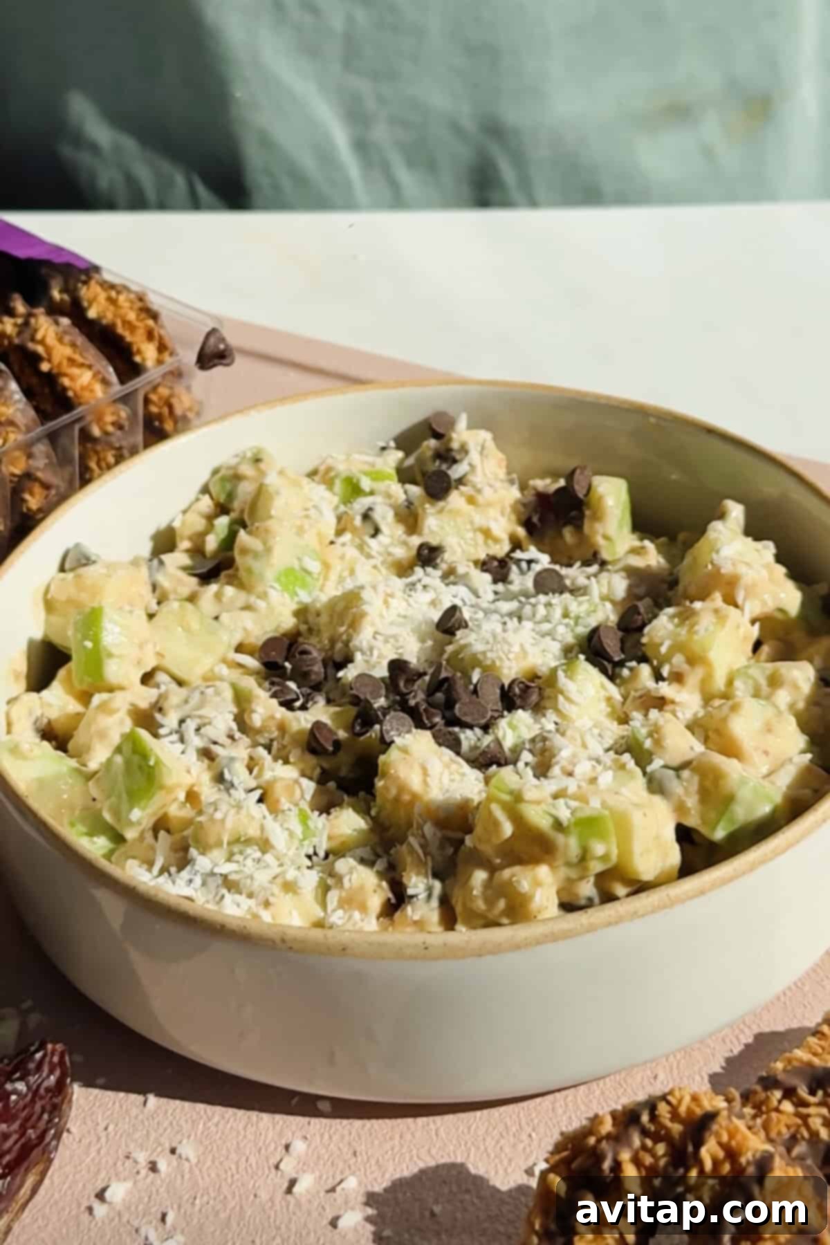 A vibrant bowl of apple salad with diced apples, shredded coconut, and chocolate chips.