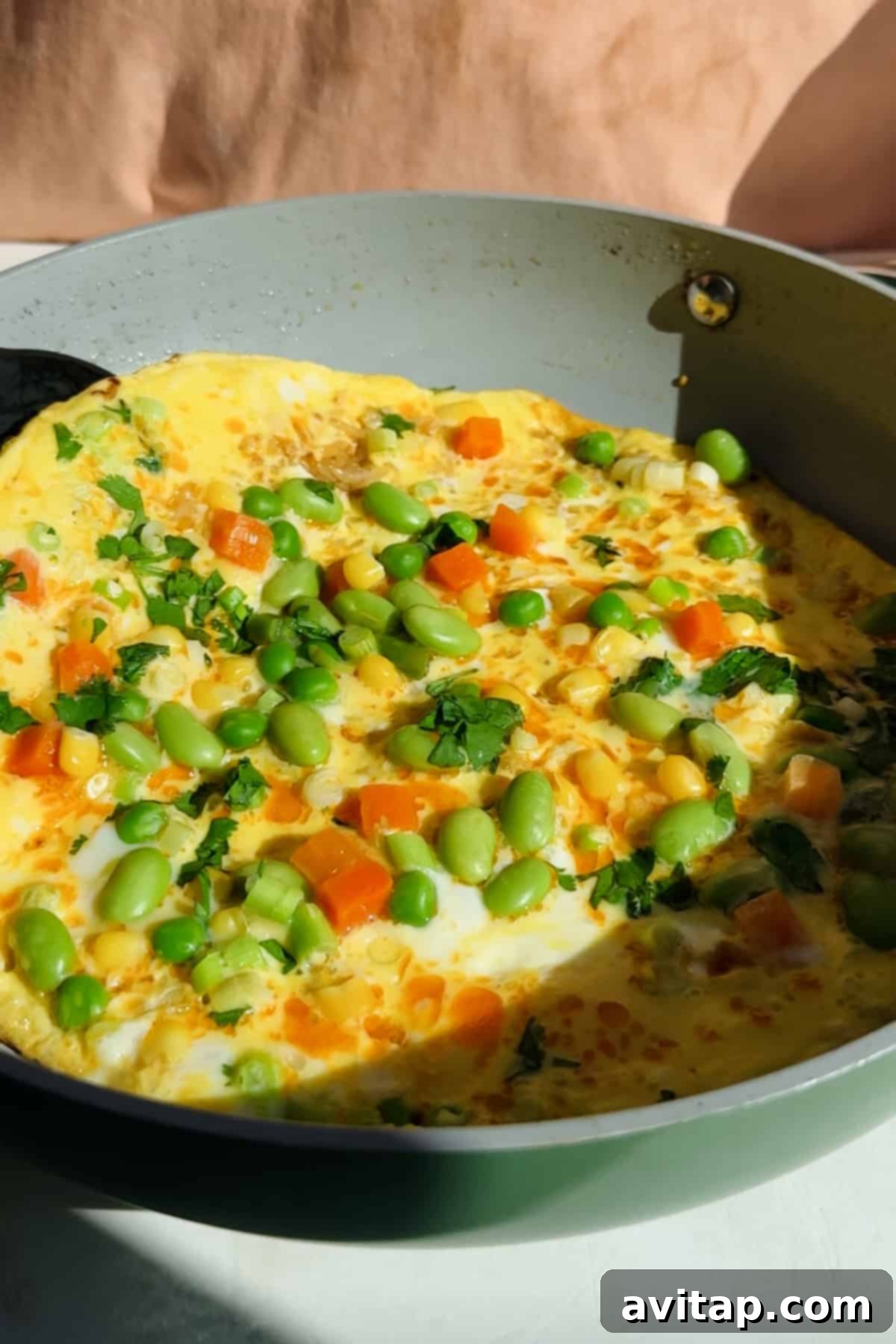 Crispy Rice Omelet Delight 3 Omelette in a pan topped with vegetables and herbs.