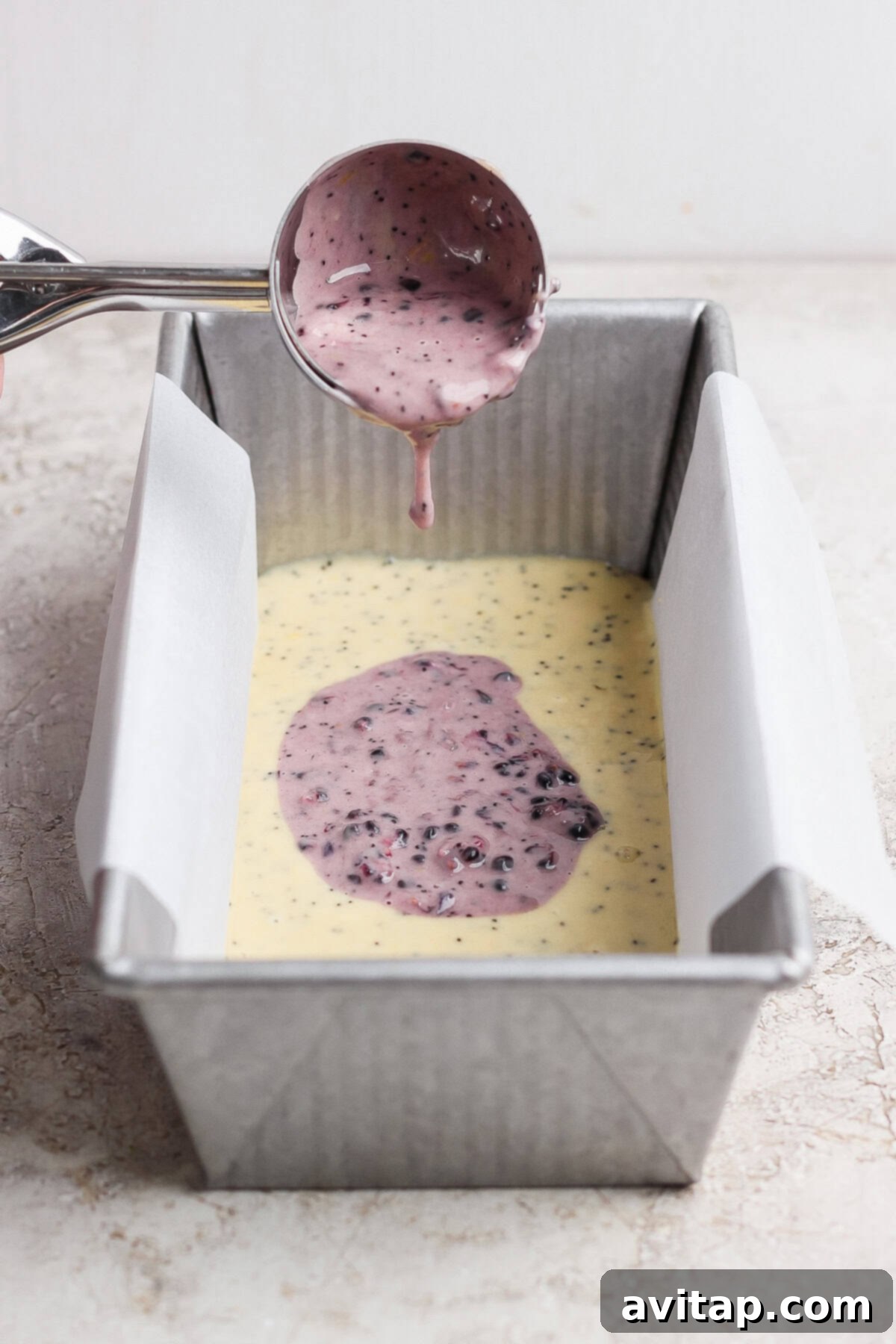 Purple berry batter being poured over yellow batter into loaf pan