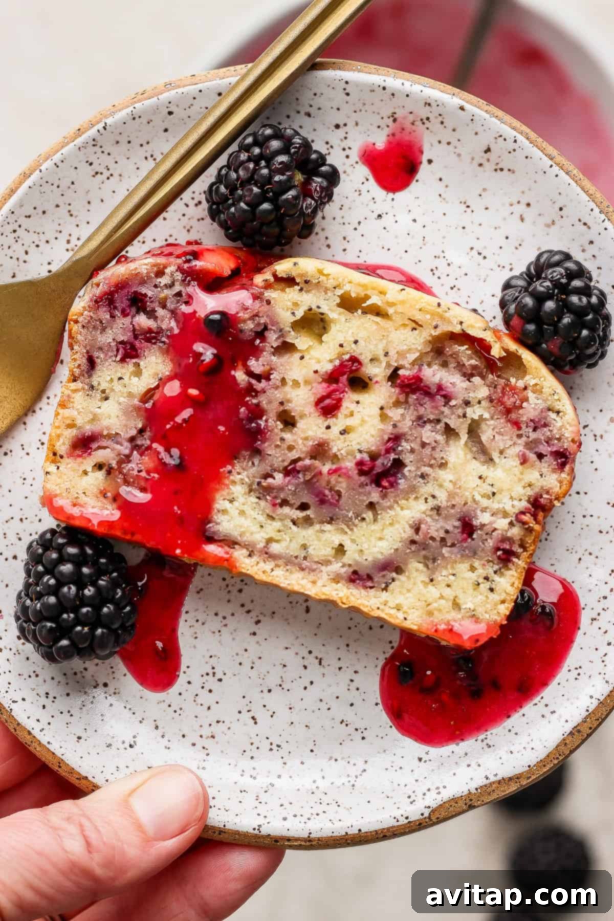 A sliced blackberry lemon poppy seed loaf with berry sauce and fresh blackberries on a plate.
