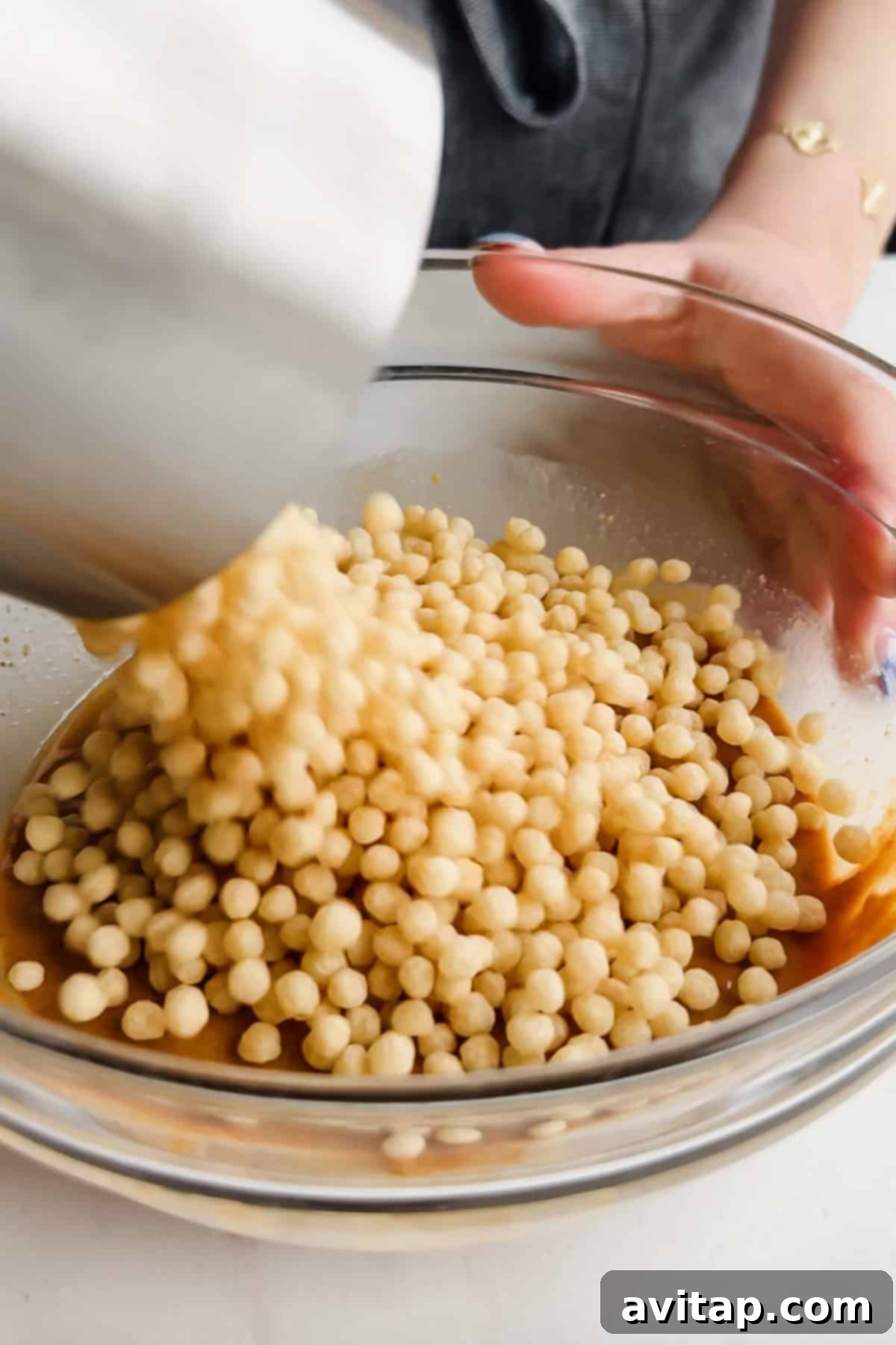 Pouring puffed quinoa into a bowl of peanut butter mixture.