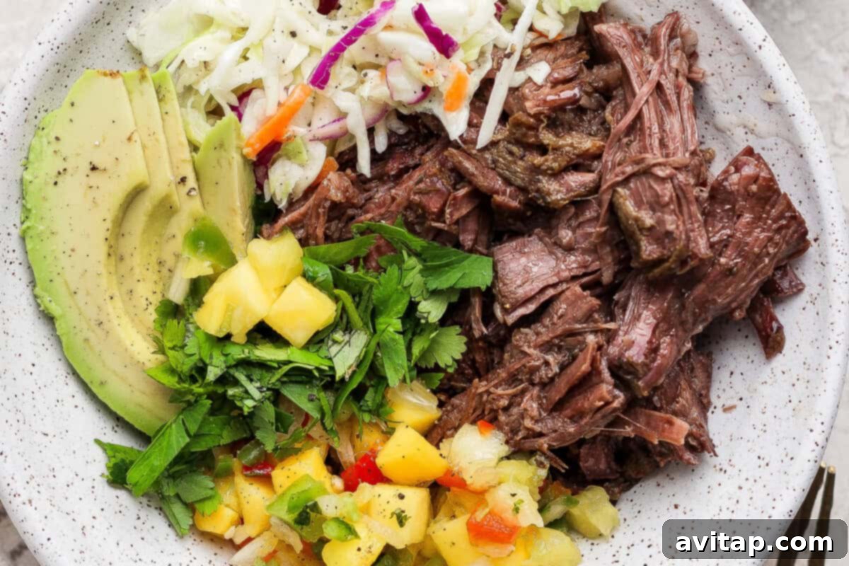 Bowl of slow cooker shredded beef with avocado, coleslaw, cilantro, and pineapple salsa
