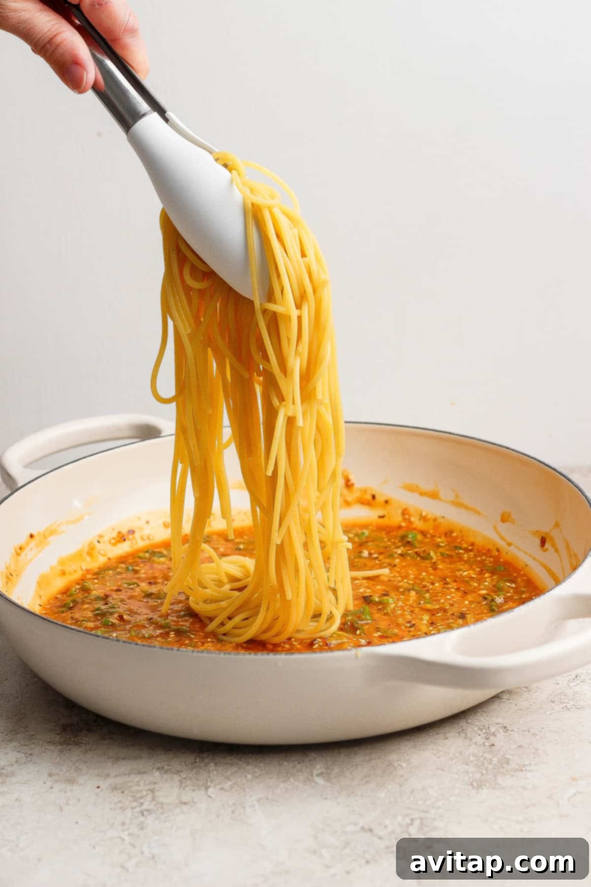 Tossing the cooked spaghetti with the chili oil sauce in a pan.