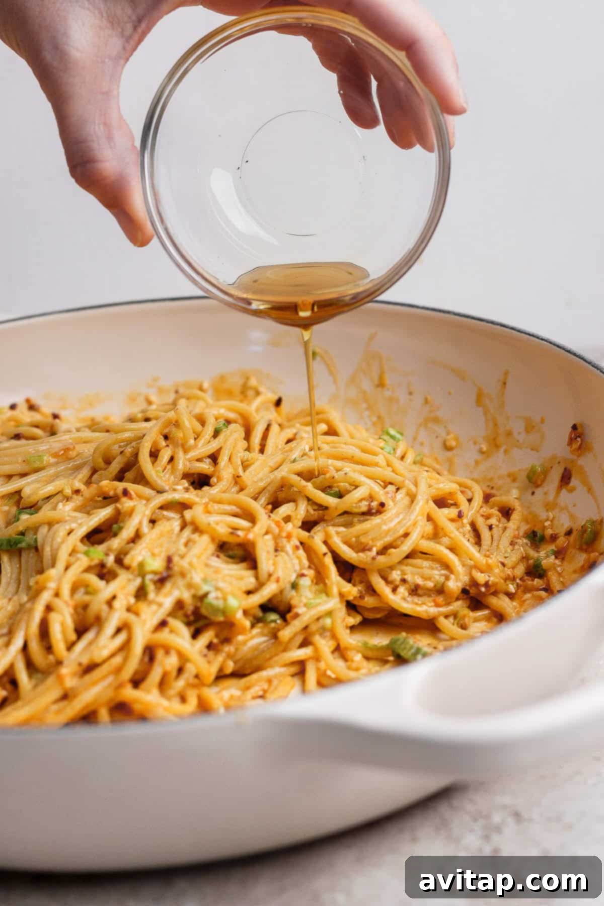 Adding the finishing touch of sesame oil to the Tahini Chili Oil Noodles.