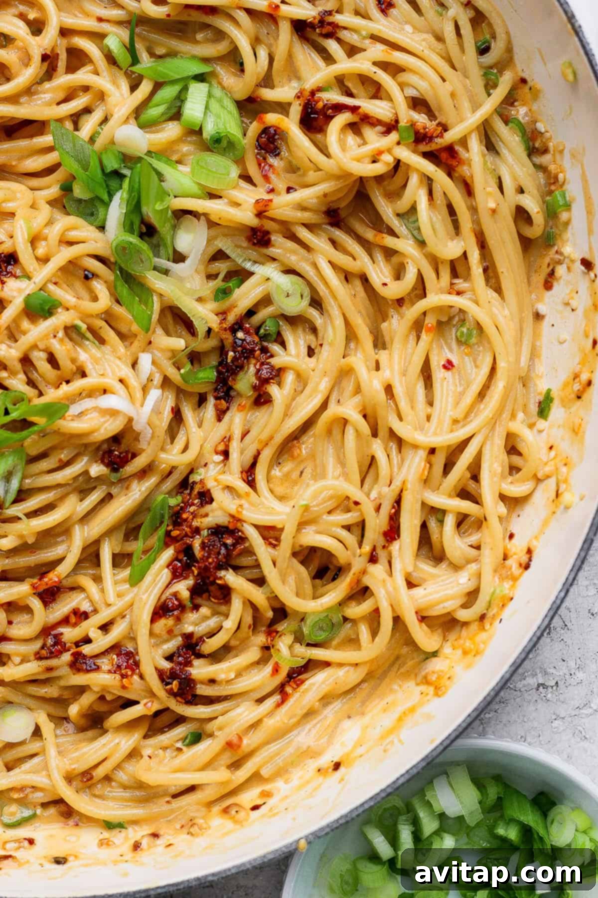 A serving of Tahini Chili Oil Noodles, garnished with chili flakes and green onions.