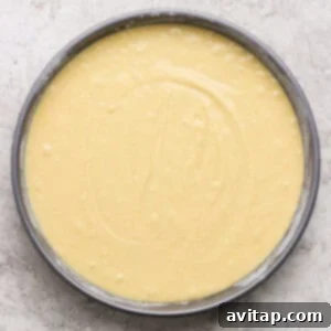 A round cake pan filled with smooth, pale yellow cake batter sits on a light textured surface.