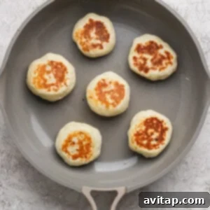Six round, golden-brown patties are cooking in a nonstick skillet on a light-colored surface.