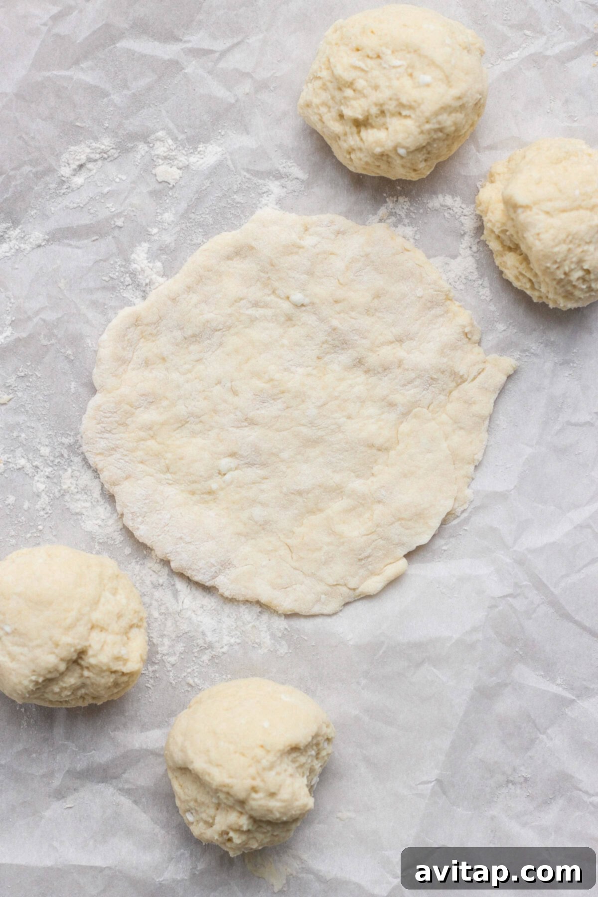 A sheet of parchment paper dusted with flour, showcasing four neatly portioned dough balls and one larger flattened round of dough, ready for filling.