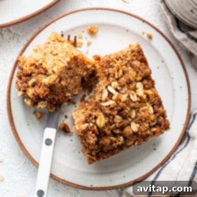 A perfectly sliced oatmeal coffee cake on a white plate, revealing its moist crumb and crumbly streusel topping, accompanied by a fork.