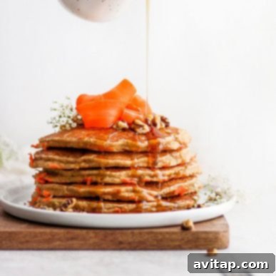 A stack of golden-brown healthy carrot cake pancakes, lightly dusted with powdered sugar, resting on a white plate, ready for a delicious breakfast.