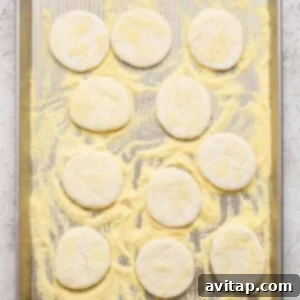 A baking sheet with twelve round, uncooked dough pieces on a layer of cornmeal, ready to be baked.