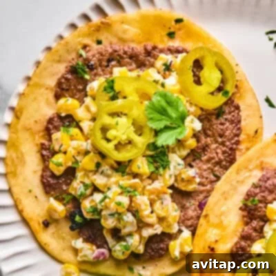 Game Changing Street Corn Recipes 3 A close-up of a delicious street corn smash taco on a white plate, topped with creamy corn and cilantro.