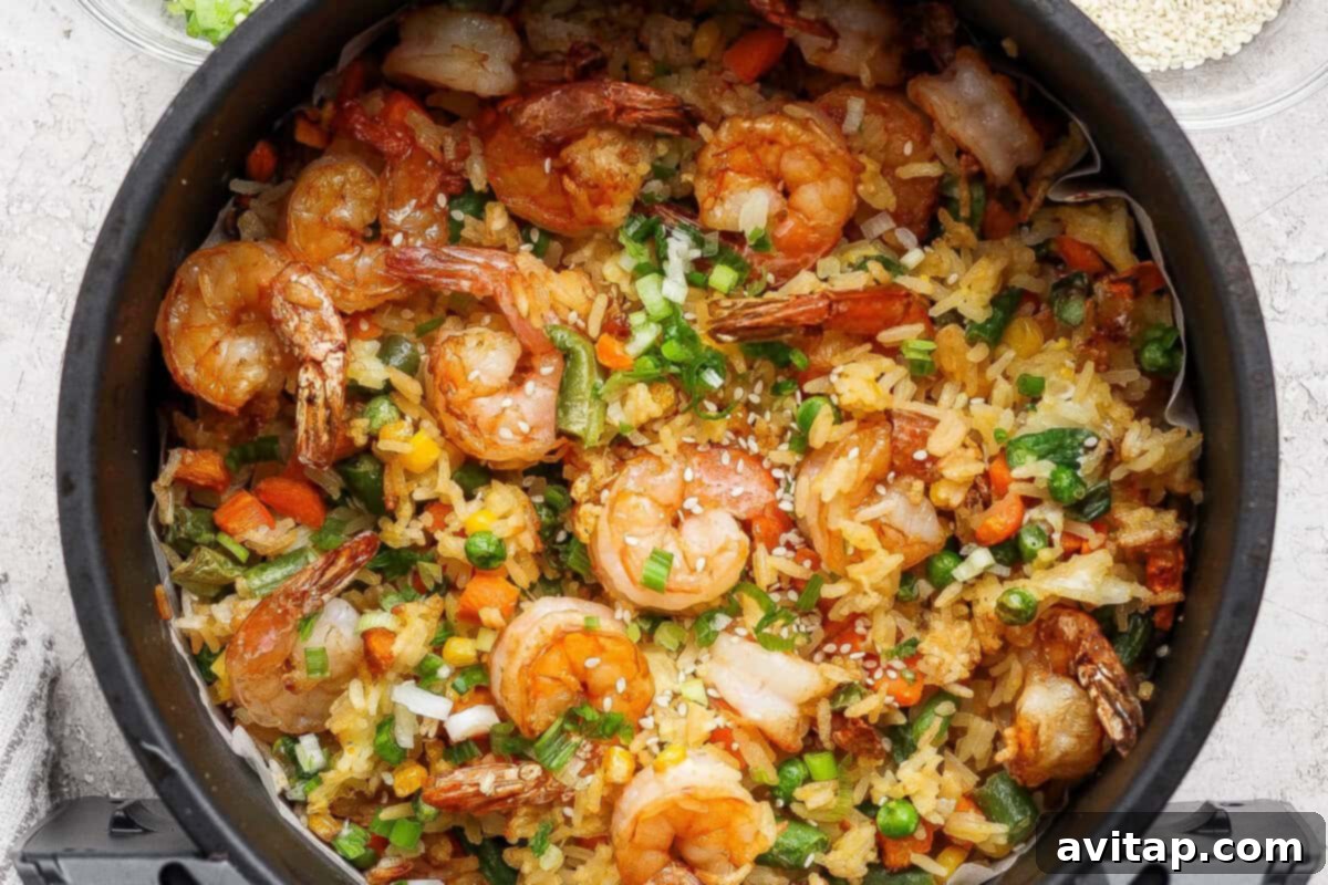 A close-up of cooked shrimp fried rice with mixed vegetables, garnished with chopped green onions, served in a black bowl.