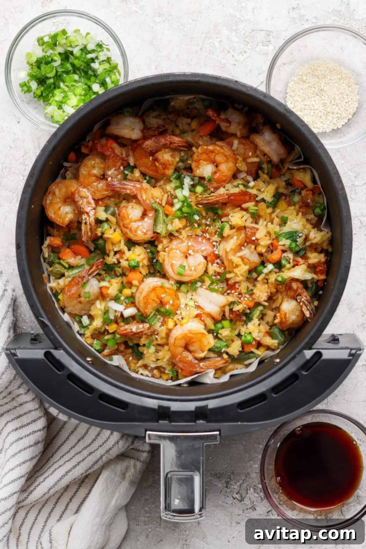 Cooked shrimp fried rice in an air fryer basket, garnished with chopped green onions.