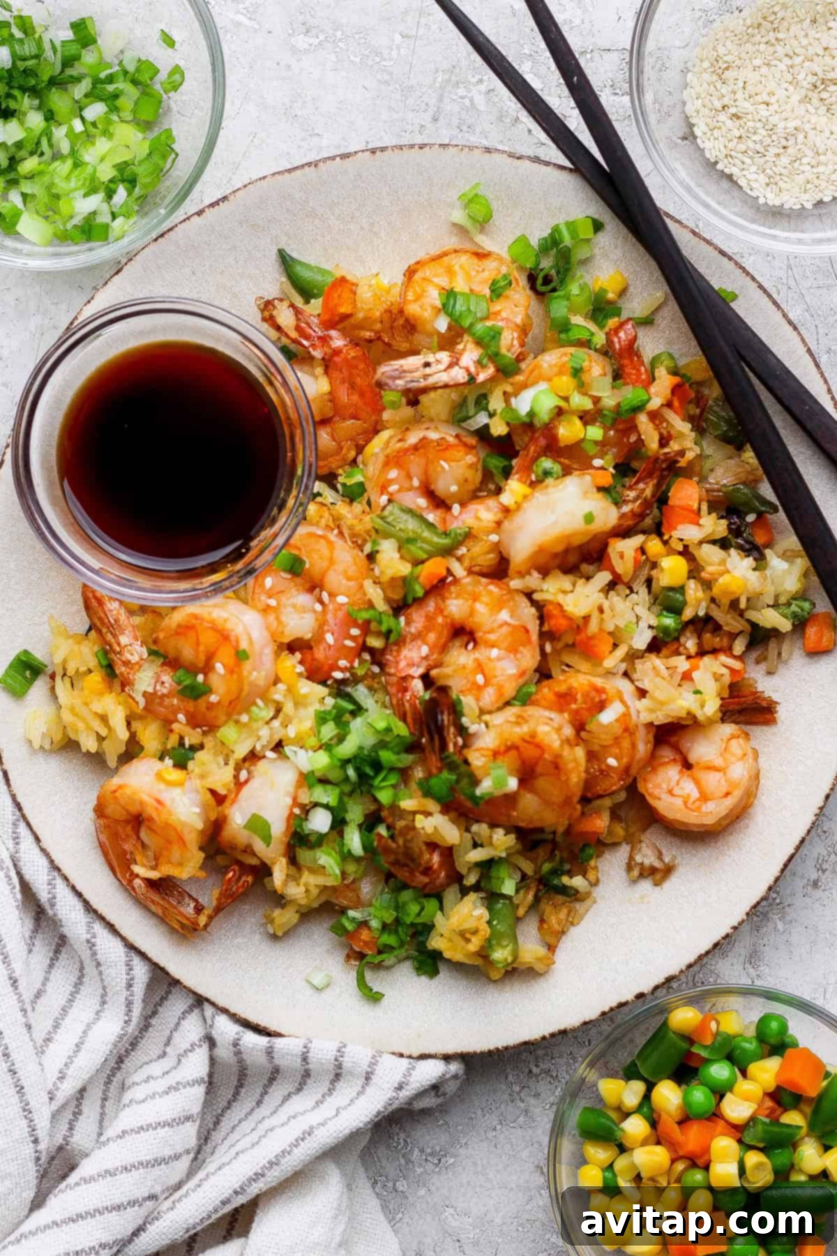 A plate of shrimp fried rice with mixed vegetables, topped with chopped green onions, served with soy sauce and chopsticks.
