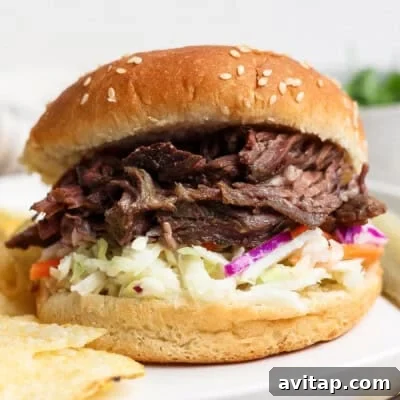 Shredded beef sandwich with coleslaw served on a sesame seed bun, with potato chips on the side.