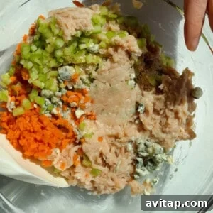 Buffalo Chicken Protein Bars — Crispy Baked Snackable Bars 11 Mixing ground chicken, carrots, celery, blue cheese crumbles, and seasonings in a glass bowl for protein bars