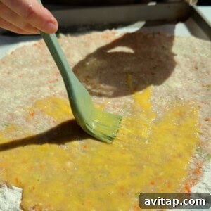 Buffalo Chicken Protein Bars — Crispy Baked Snackable Bars 13 Brushing egg wash over chicken protein bar mixture on a floured parchment-lined surface