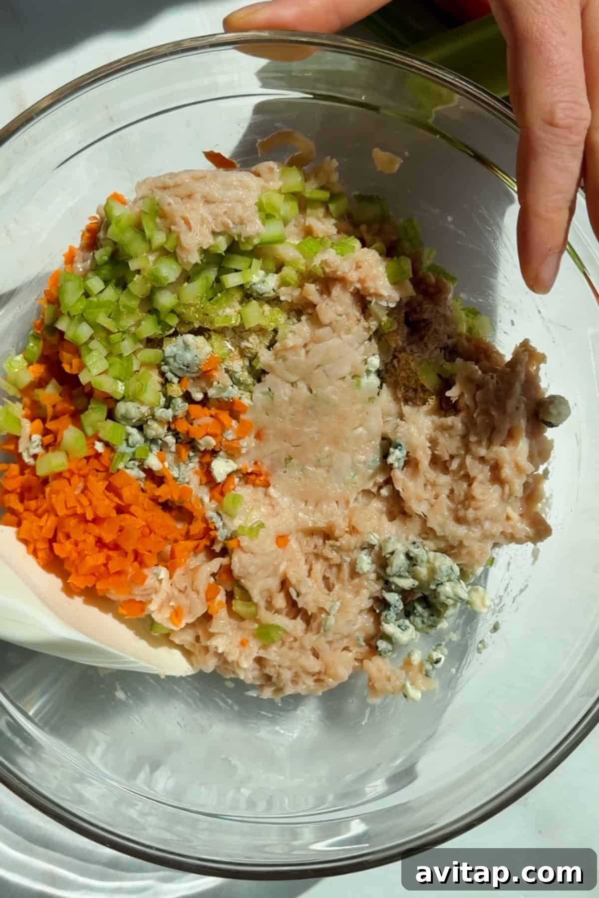 Buffalo Chicken Protein Bars — Crispy Baked Snackable Bars 4 Mixing ground chicken, carrots, celery, blue cheese crumbles, and seasonings in a glass bowl for protein bars