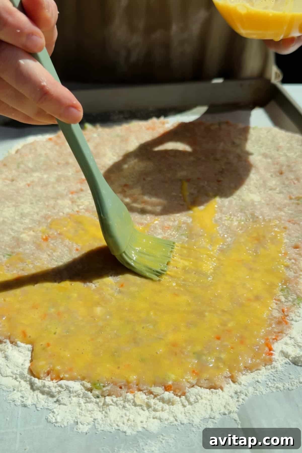 Buffalo Chicken Protein Bars — Crispy Baked Snackable Bars 6 Brushing egg wash over chicken protein bar mixture on a floured parchment-lined surface
