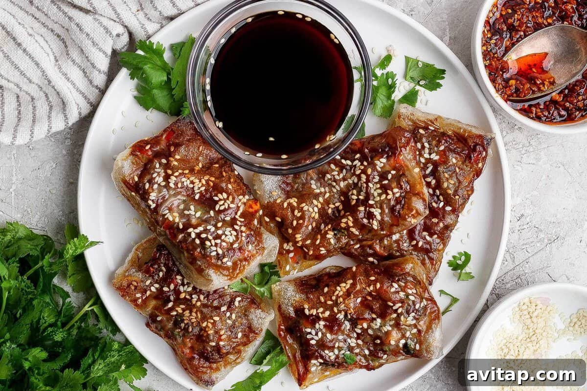 A white plate with five pieces of crispy, glazed tofu topped with sesame seeds, garnished with cilantro, and served with a small bowl of dark dipping sauce.
