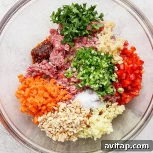 A glass bowl containing ground meat, chopped carrots, bell peppers, mushrooms, parsley, ginger, garlic, green onions, and seasonings arranged in separate piles.