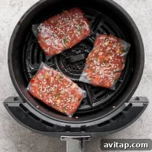 Three uncooked frozen salmon filets coated with marinade and sesame seeds arranged in the basket of an air fryer.