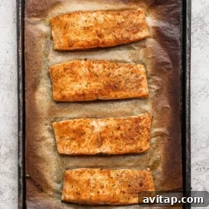Four golden broiled salmon fillets on a parchment-lined baking sheet fresh from the oven.