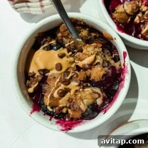 A bowl of berry crumble topped with peanut butter, chocolate chips, and a spoon resting inside.