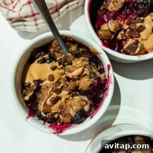 Three small white ramekins filled with baked berry dessert, topped with peanut butter and chocolate chips, with metal spoons and a red-striped cloth nearby.