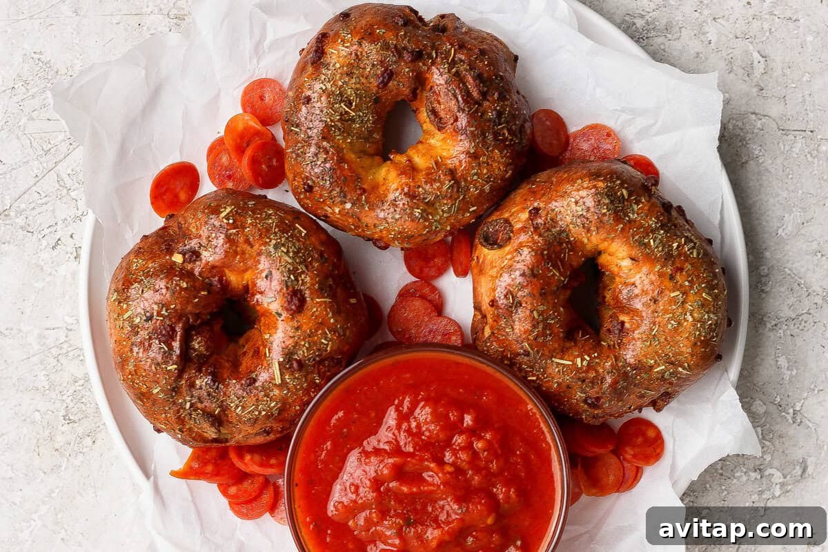 Three pizza protein bagels on parchment paper served with marinara sauce and pepperoni