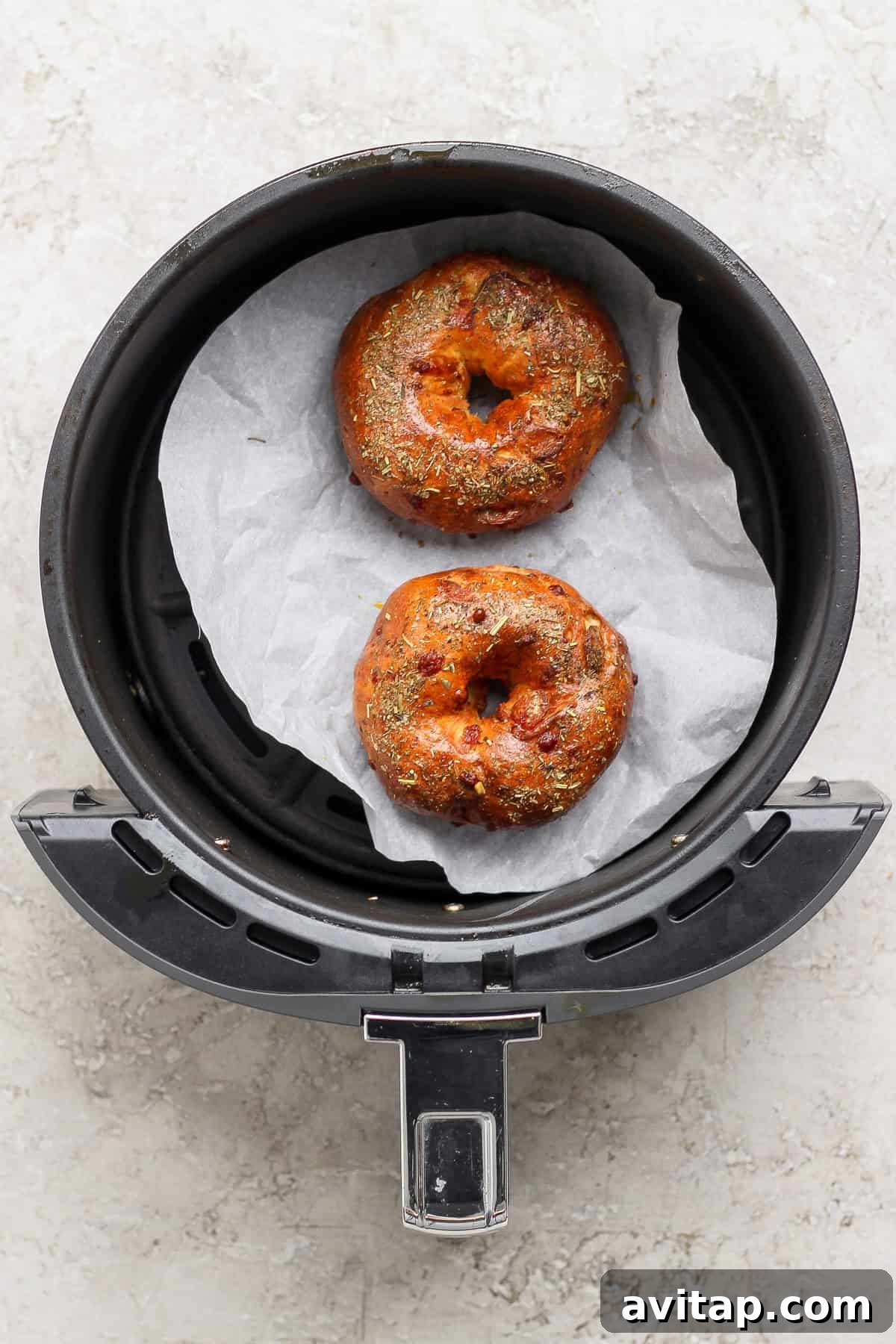 Two baked pizza protein bagels with Italian seasoning in an air fryer basket