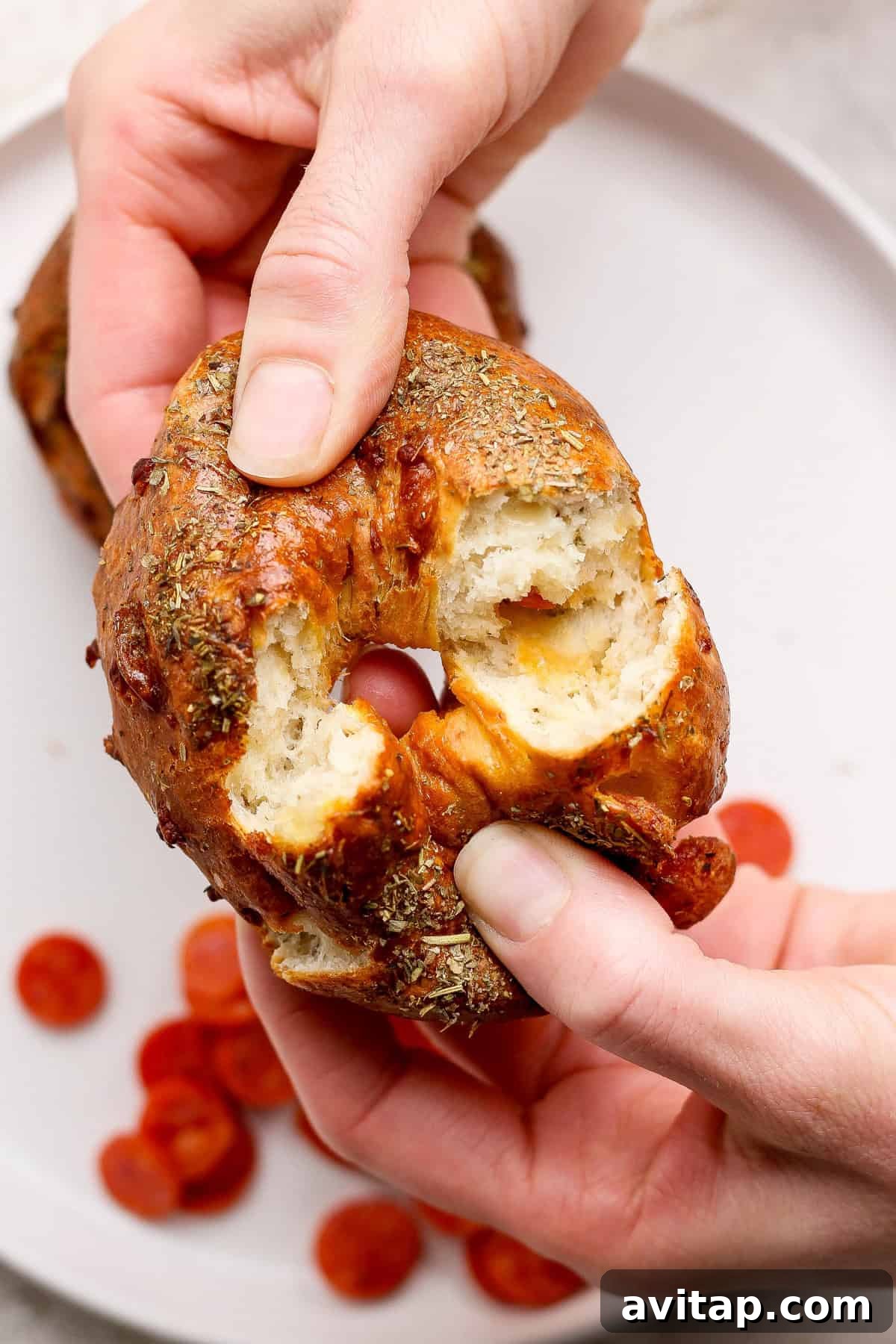 Two hands pulling apart a pizza protein bagel to show the pepperoni inside